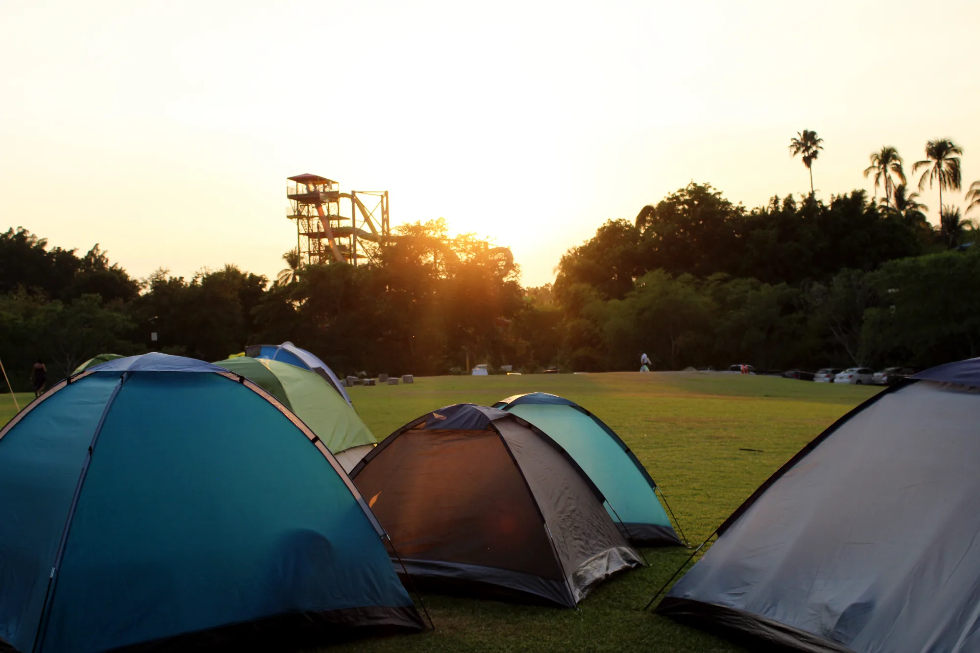 Tiendas de campaña sobre el pasto al atardecer, con los toboganes del parque de fondo