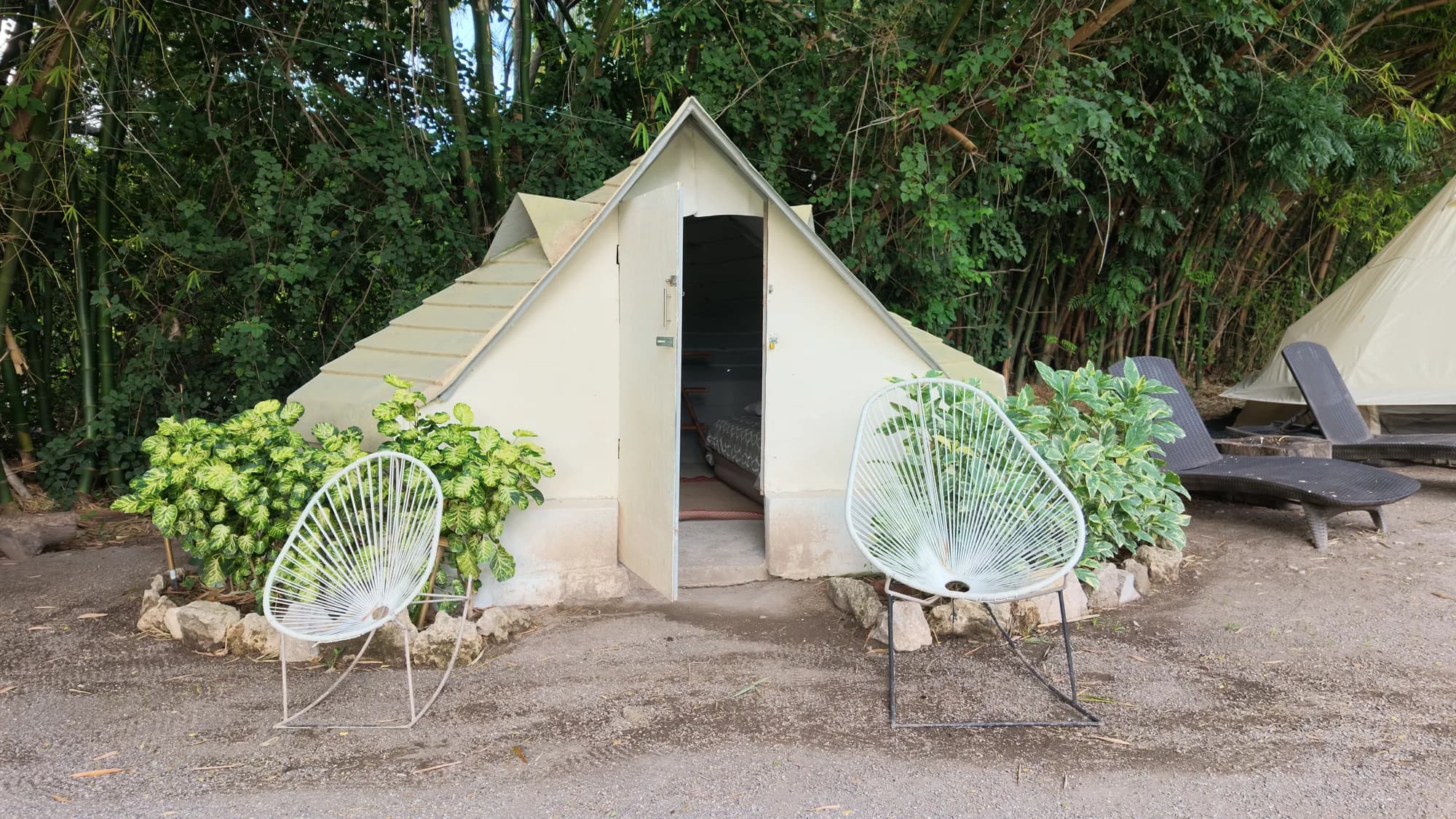 Tienda de glamping tipo cabaña de lona con sillas Acapulco a la entrada, entre bambú